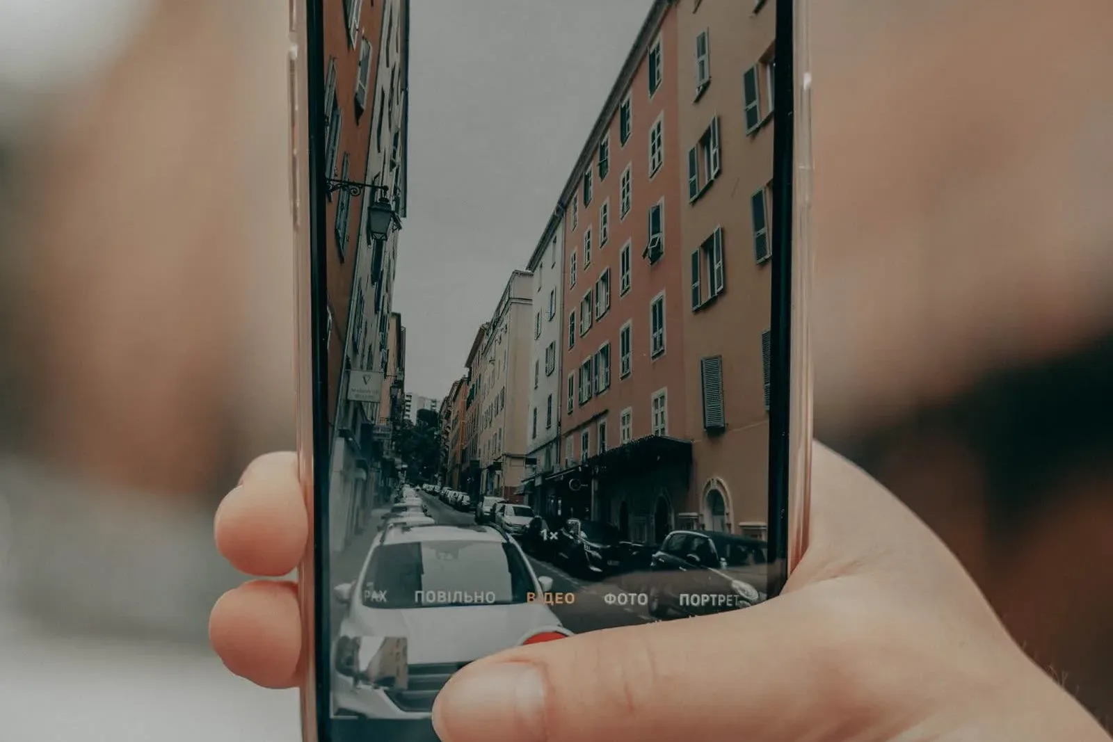 Dłoń trzyma telefon w trybie nagrywania wideo i filmuje ulicę z kamienicami: tak wygląda weryfikacja wideo profilu firmy