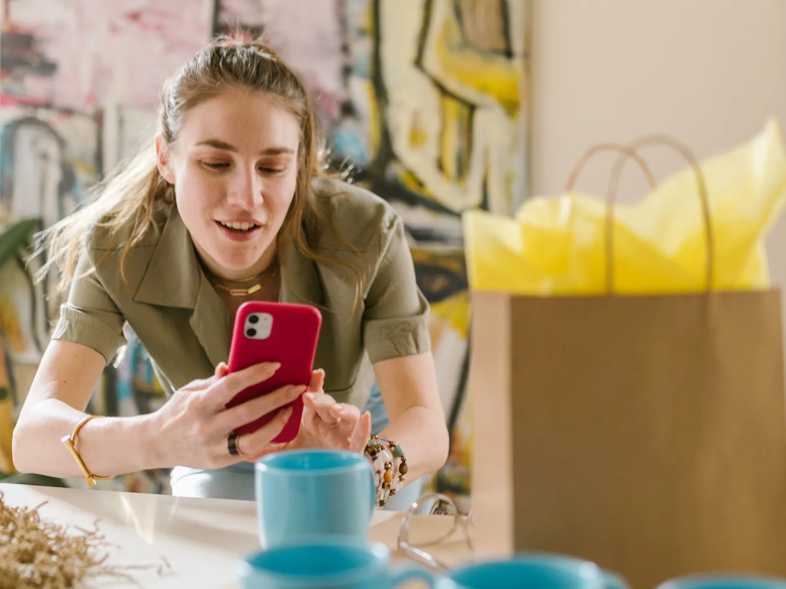 A woman leans over a table and photographs blue mugs with her phone