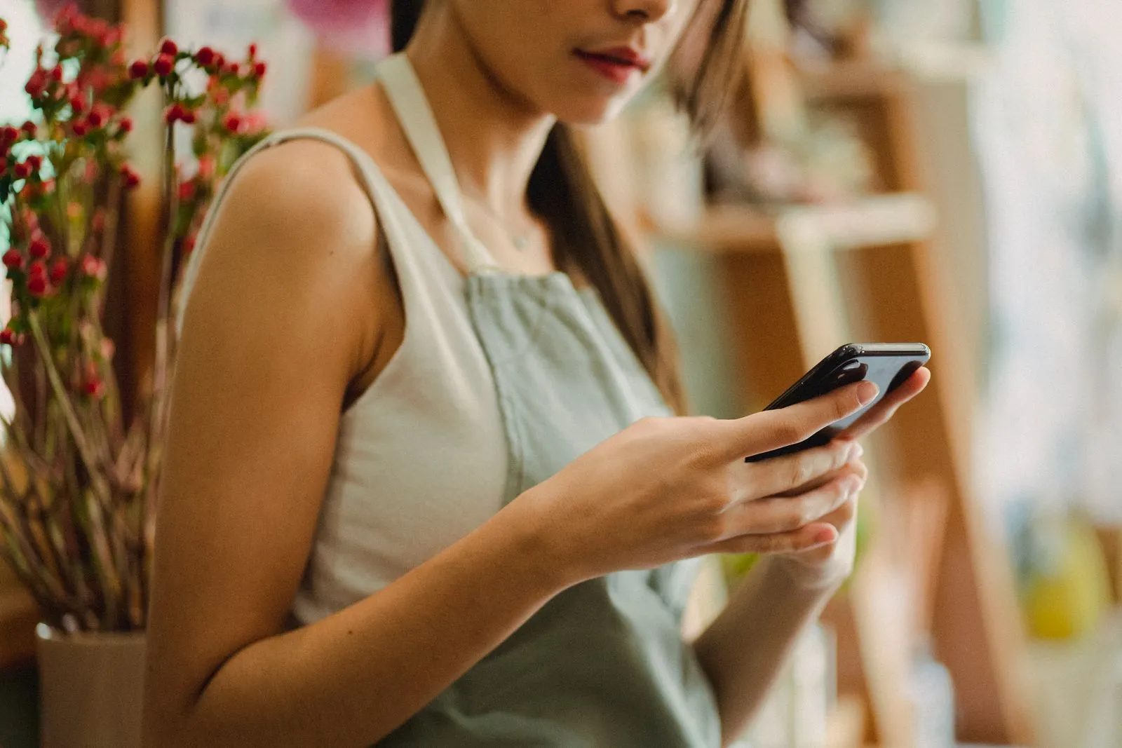 A florist in a grey apron checks her phone inside a flower shop