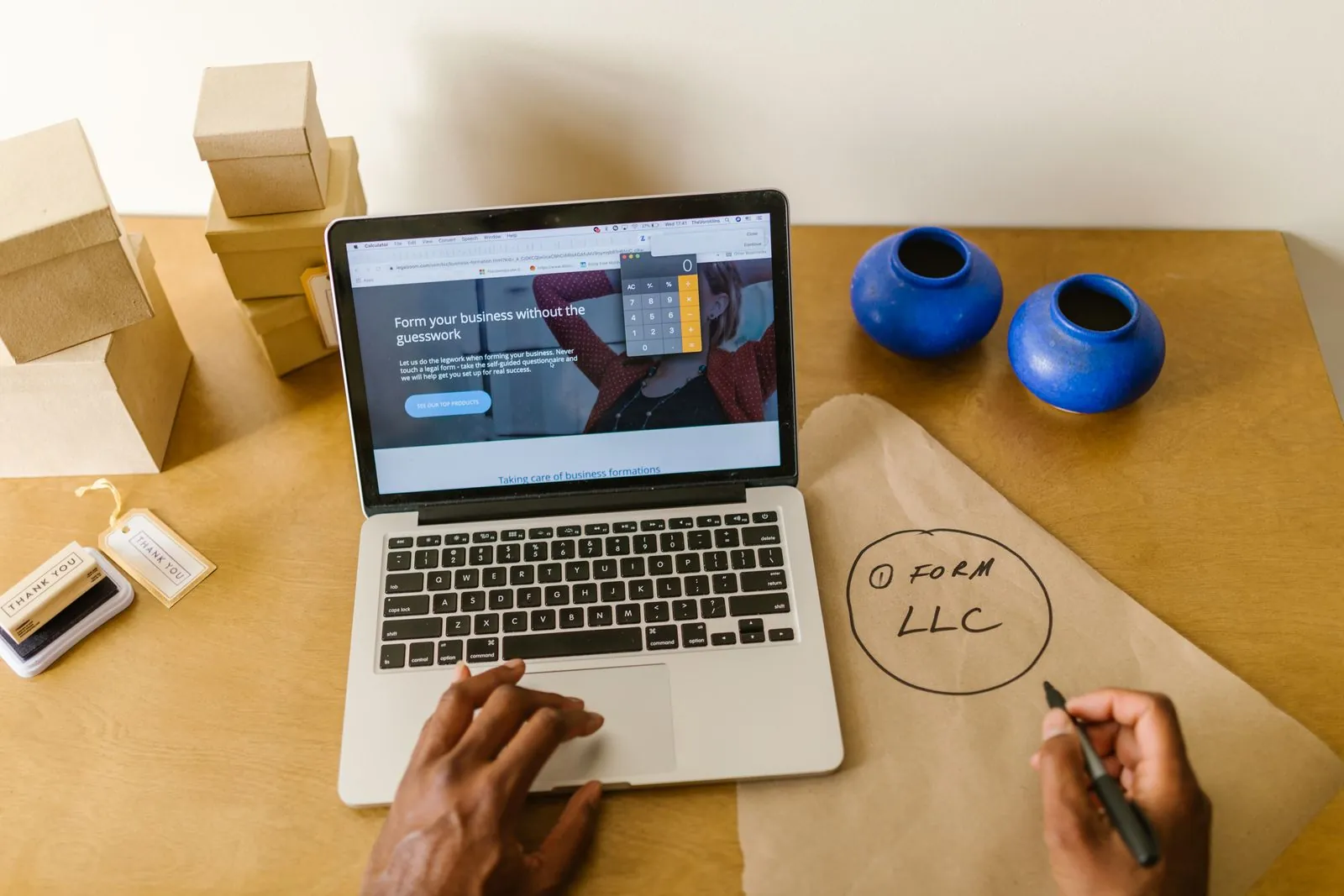 A laptop open on a business website on a craft-paper desk while a hand sketches a plan
